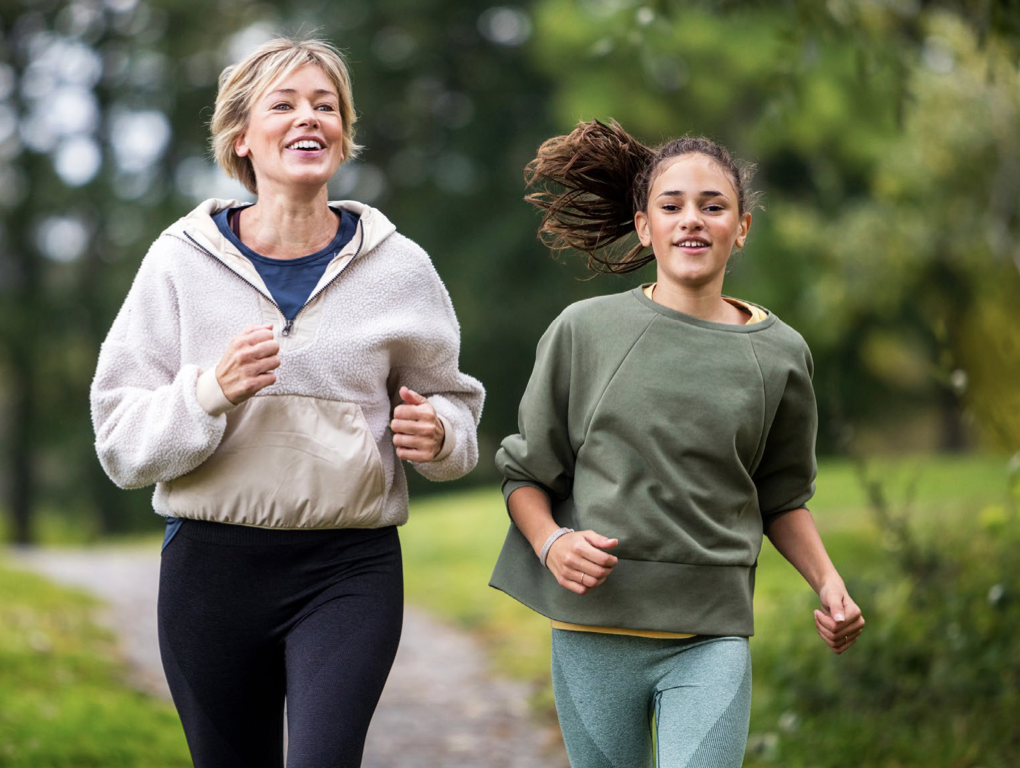 A mom and her daughter jogging on a path.