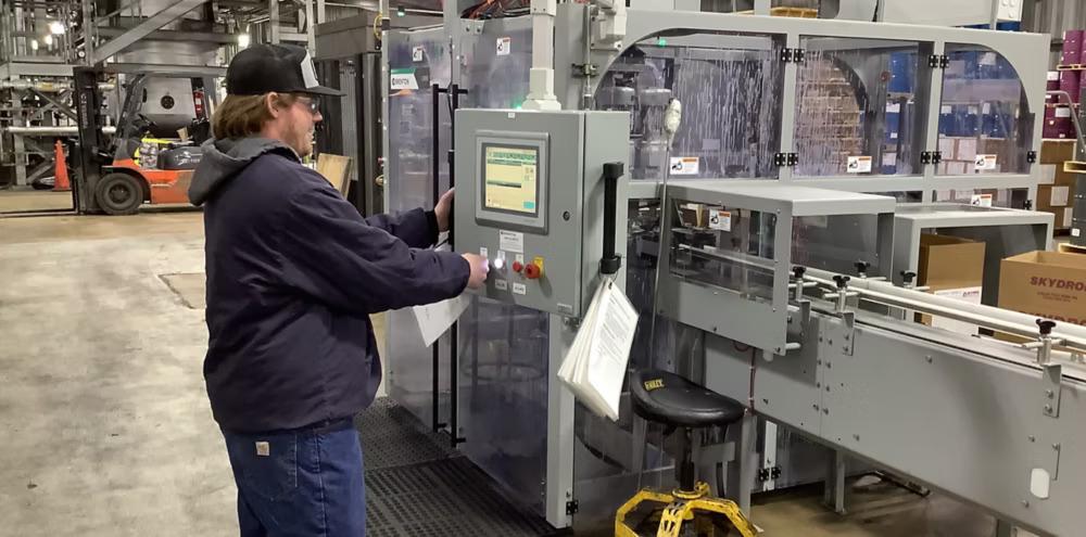 A person pushing a button on a box on front of a large CNC type machine.