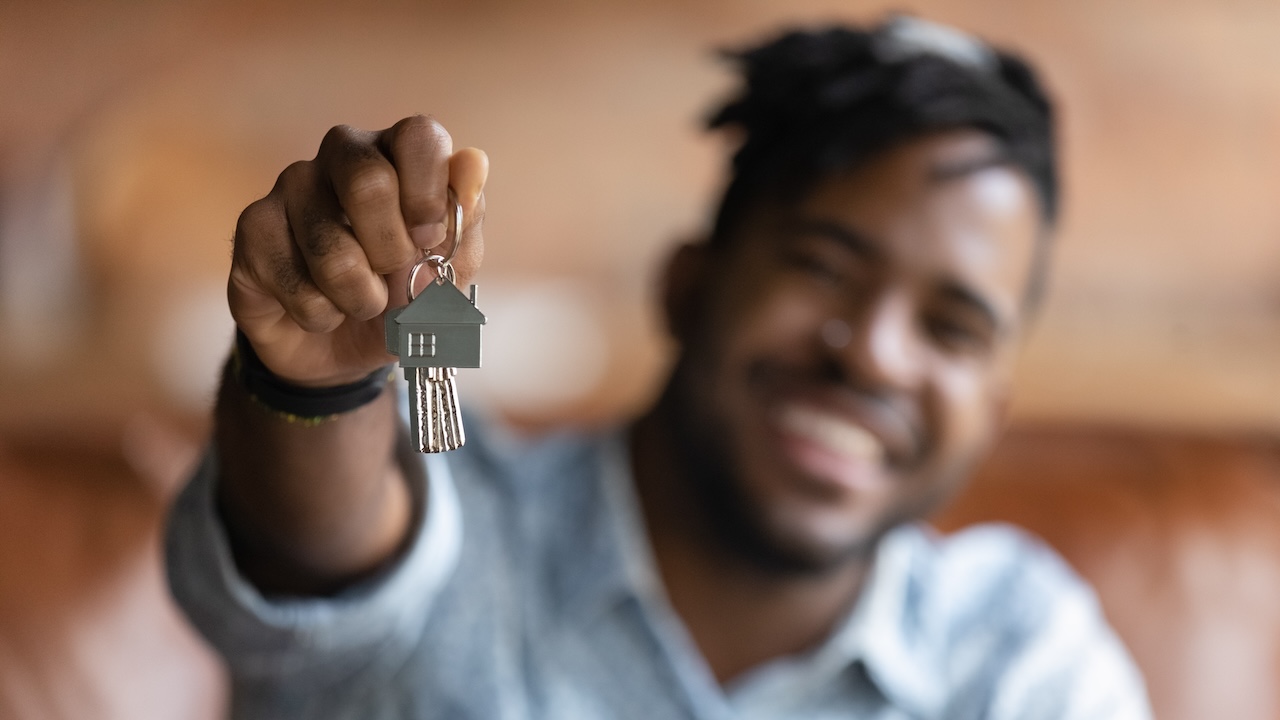 A person is holding a key chain with house keys and is smiling.