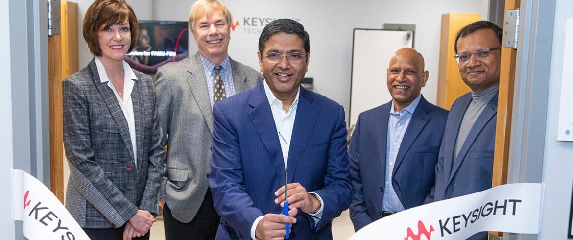 Five people in a door way, the middle person holding scissors having just cut a ribbon with Keysight logos on it.