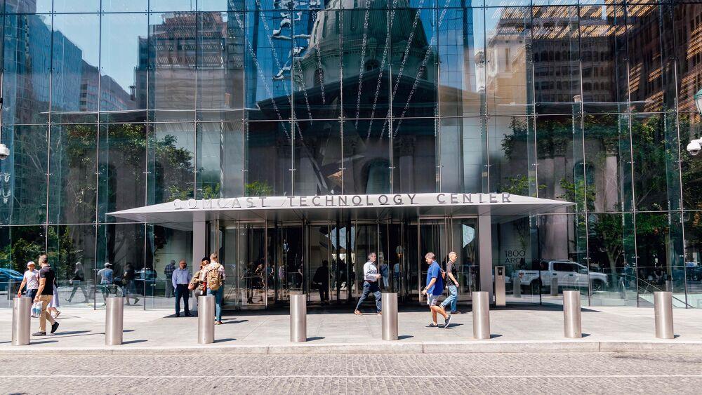 Exterior of the entry doors to "Comcast technology center." people walking by.