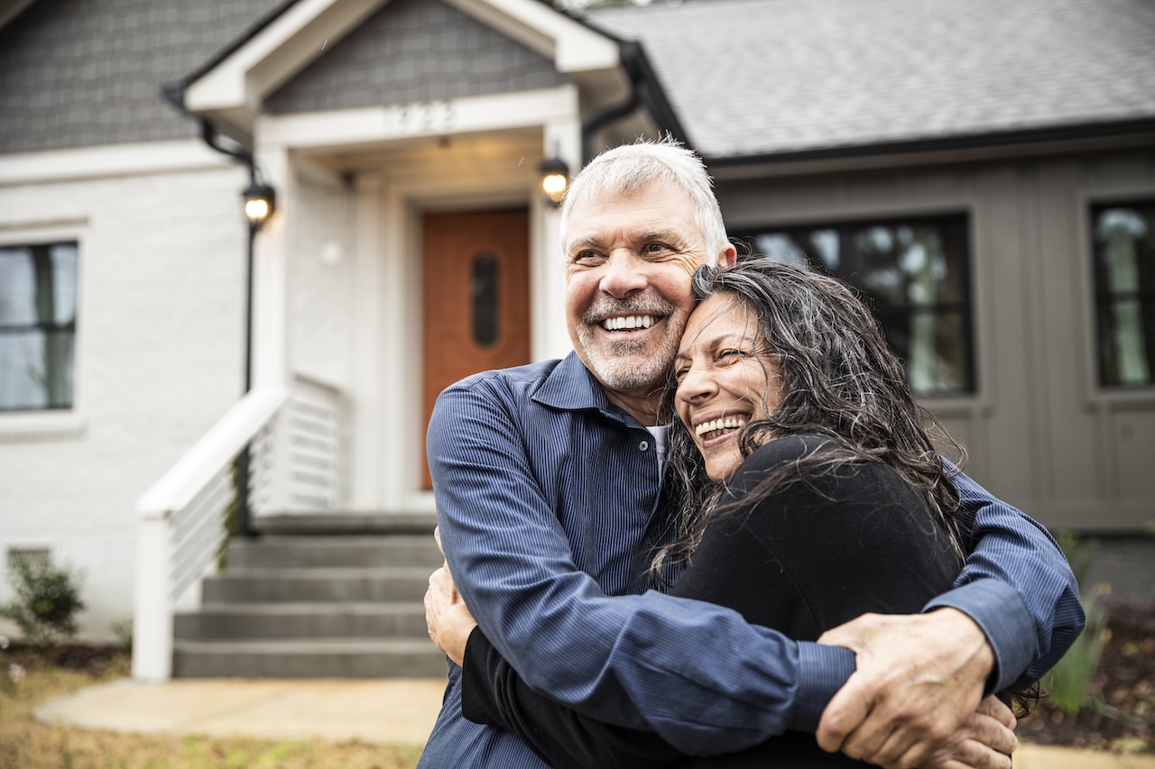 Young couple hugging in front of their new home.