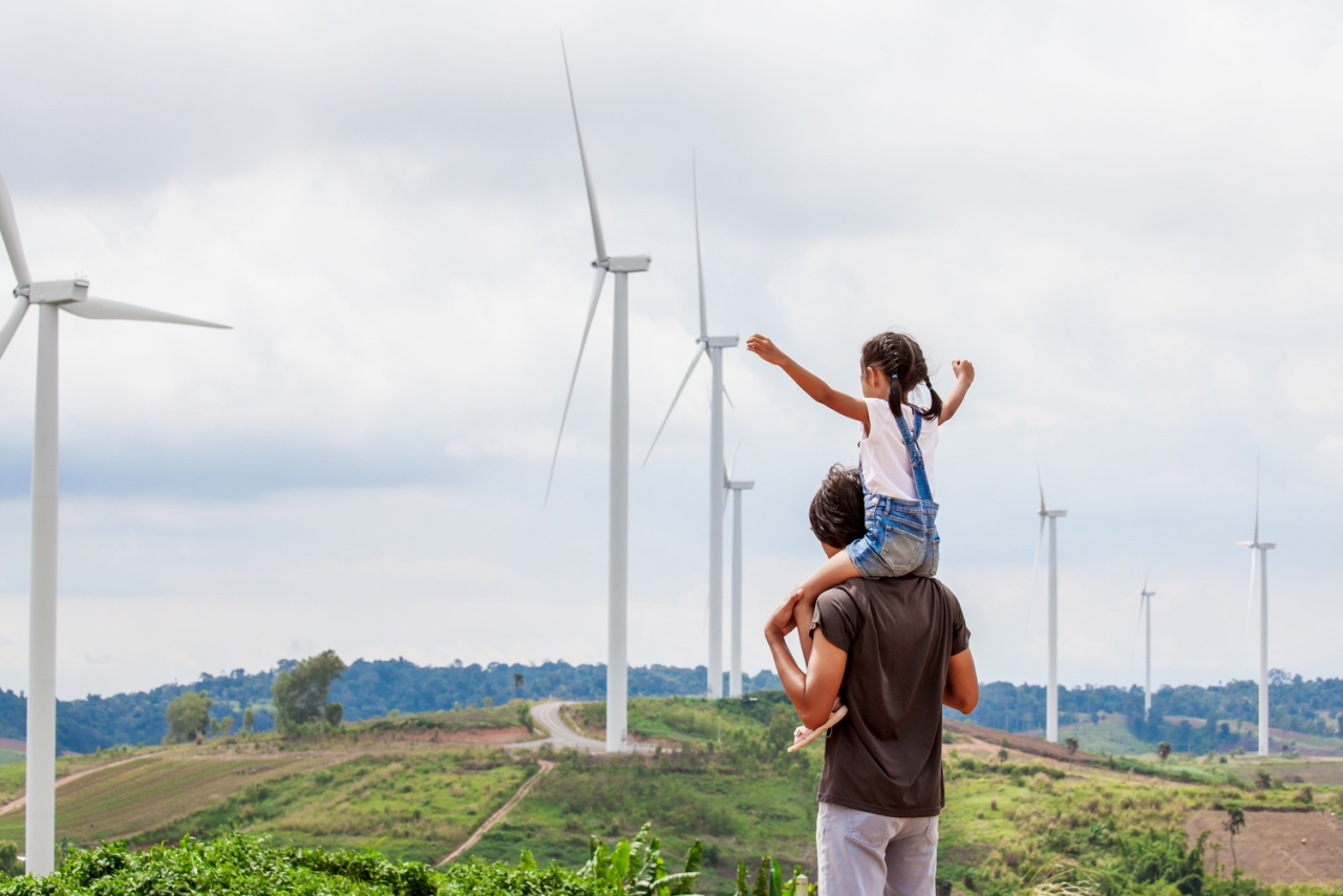 Man and child stand if front of windmills