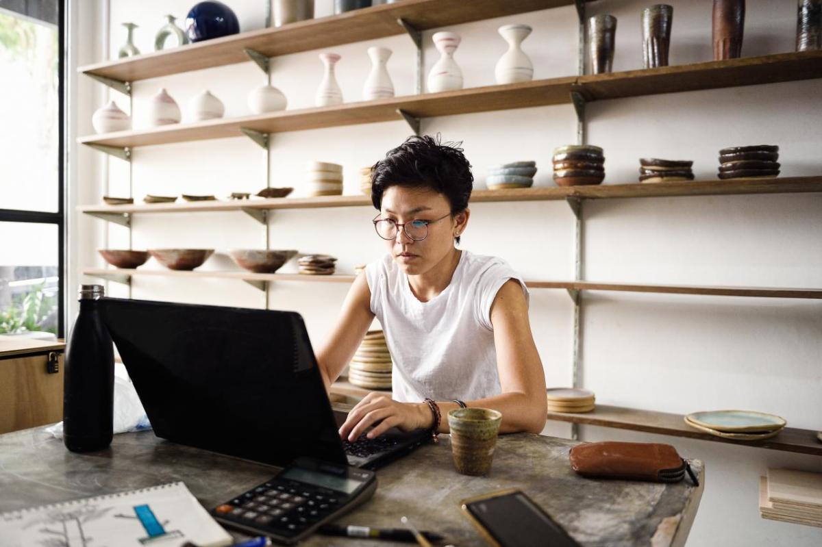 A person working on a laptop, shelves of ceramics behind them.