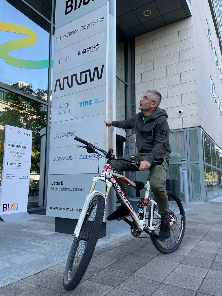 Giuliano Rapetti on a bicycle, pointing to a sign for Arrow.