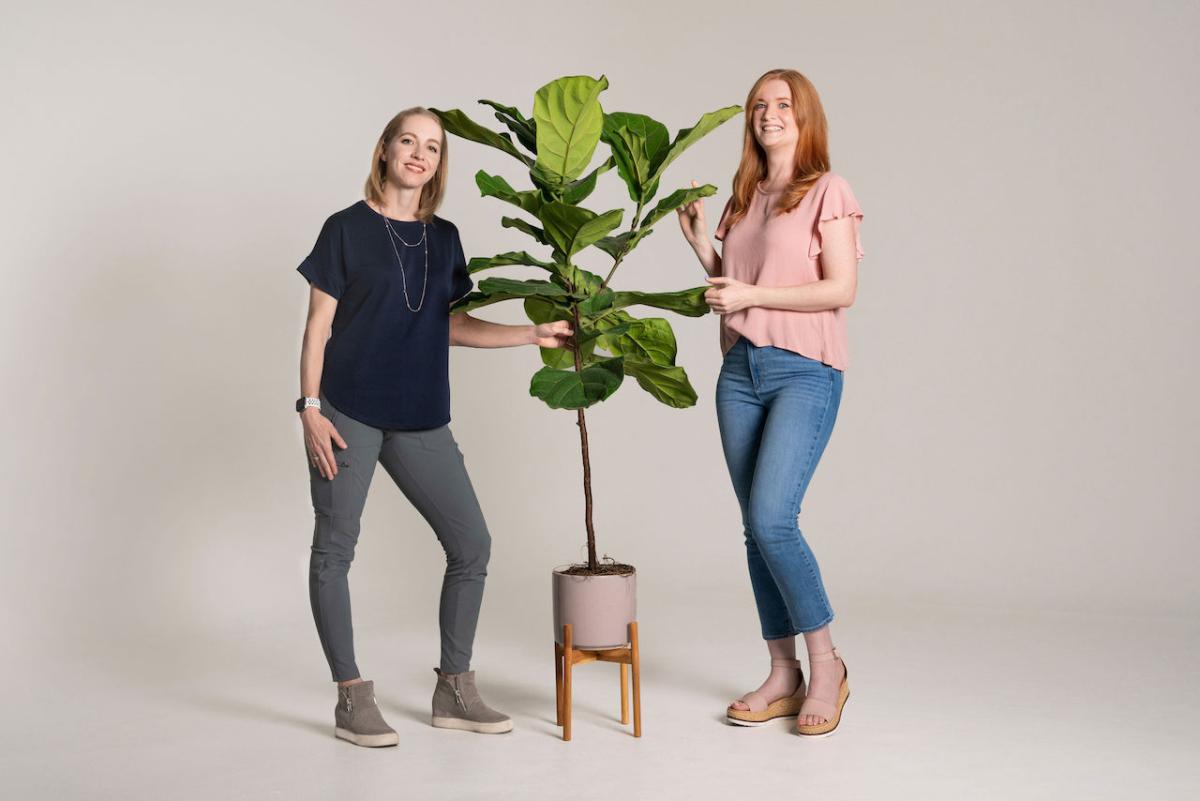 Two women standing in front of a plant.