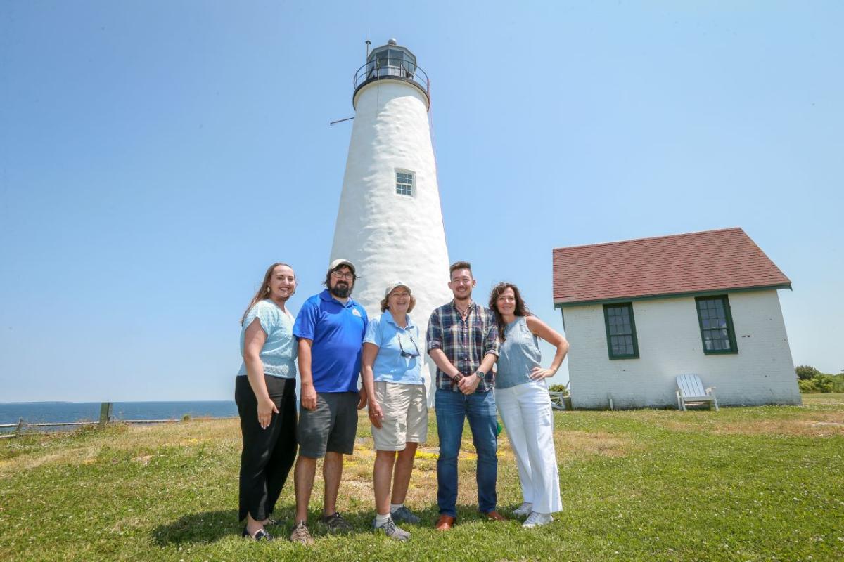 A group of five people pose in front of the island's lighthouse.