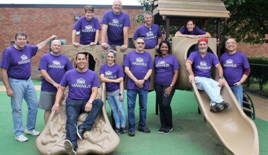 A group of people stood around a children's climbing frame, wearing purple MAXIMUS t-shirts
