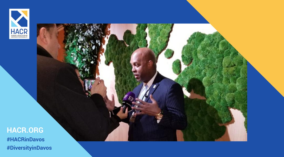 Photo of Cid Wilson, President and CEO of the Hispanic Association on Corporate Responsibility dressed in a suit speaking into a microphone with a textured, green and white wall in the background