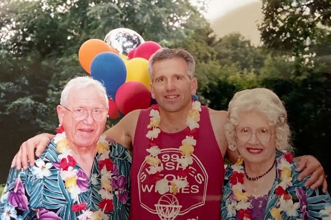 Henry Rodrique and his parents outside, wearing colorful leis, balloons behind them