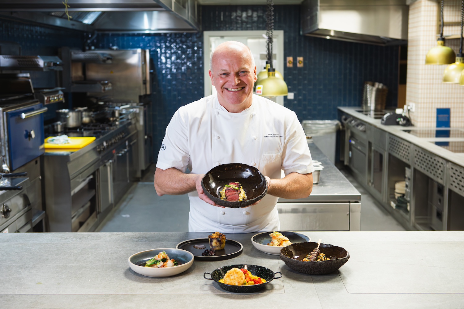 Paul Bates, executive head chef at Hilton London Metropole, holds up a dish from the zero food waste pilot menu and smiles at the camera.