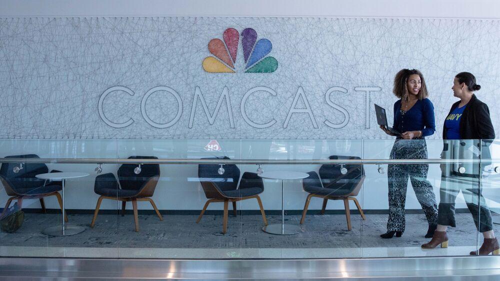Two people walking a hallway in front of a large Comcast sign
