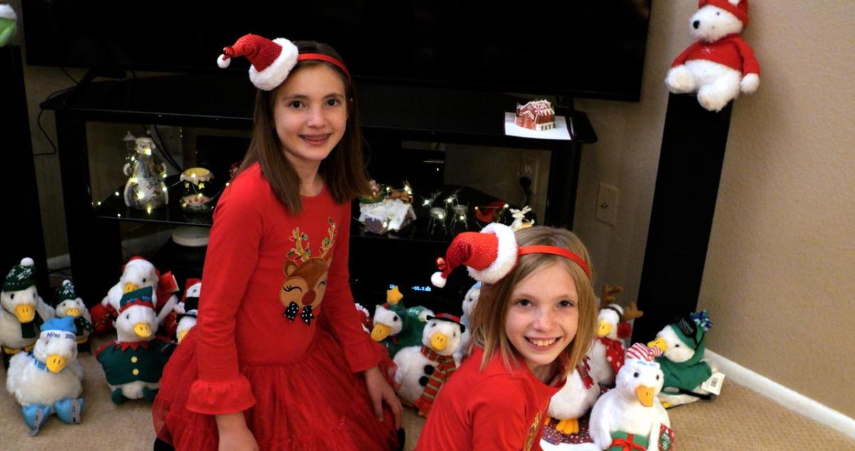 Two girls shown wearing Santa hats with the Aflac Holiday Ducks.