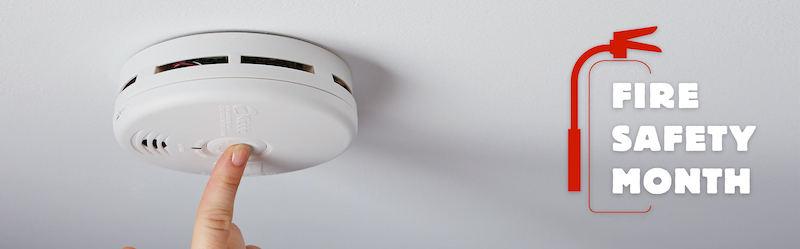 Fire Safety Month: Finger shown pushing the button on a smoke detector.