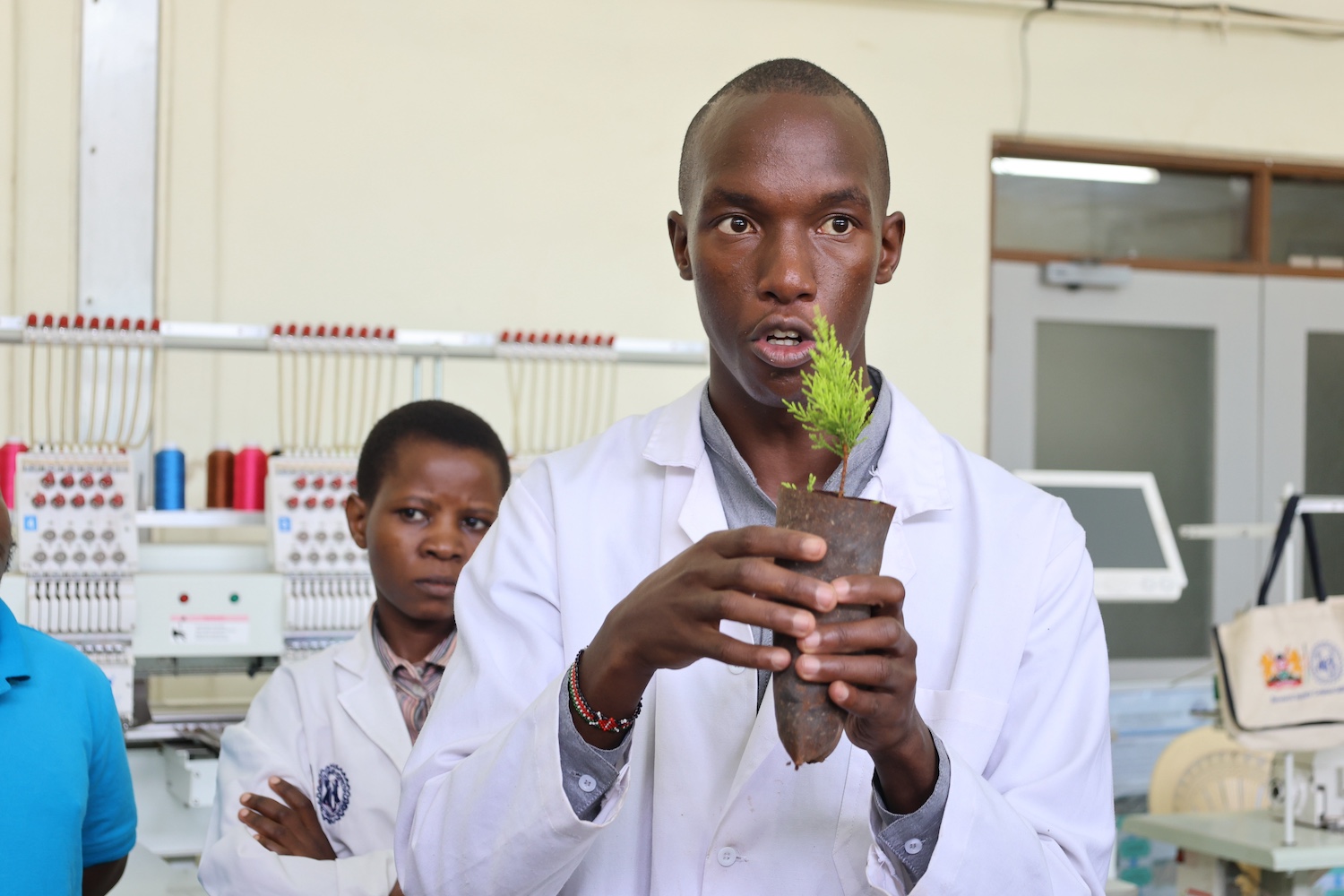 Joseph Nguthiru holds up a seedling wrapper created from dried water hyacinth with a small plant inside. 