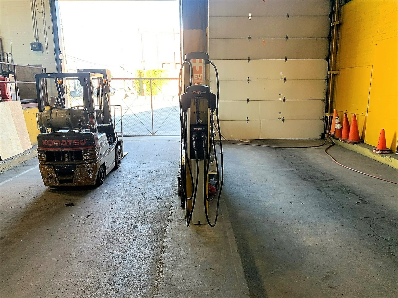 EV charger hanging in a warehouse with one garage door open behind it