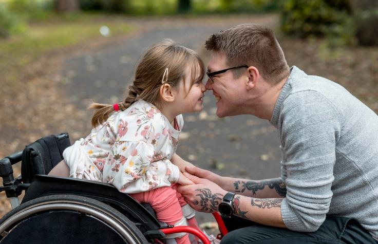 Young girl in a wheel chair with her dad hugging her.