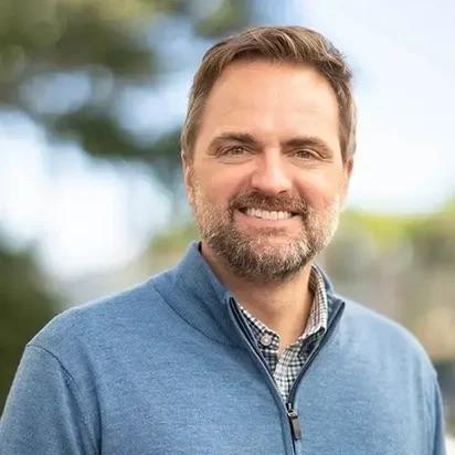 A headshot of a person wearing a blue zip sweater