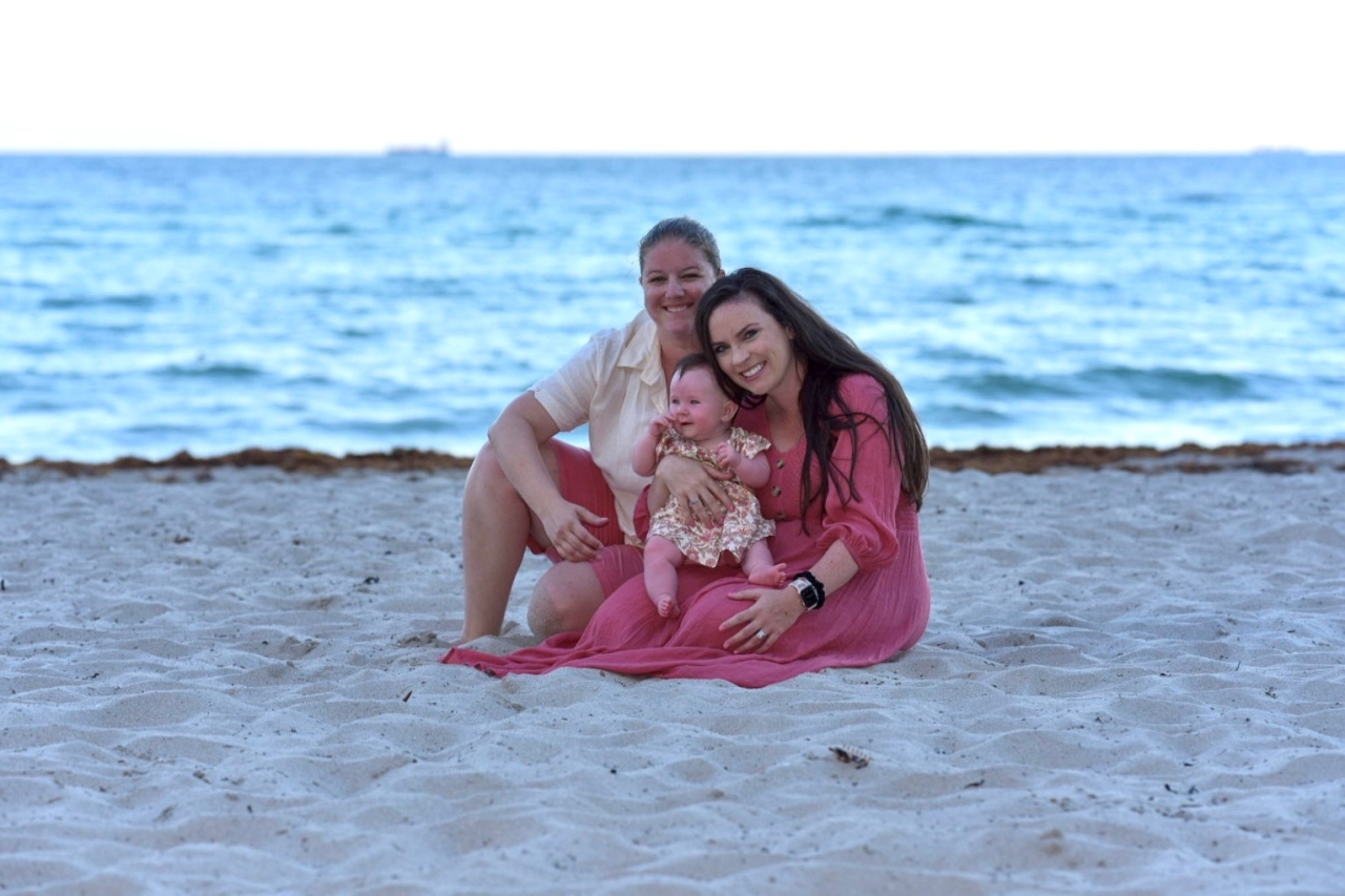 Kathryn and Emily holding their child sitting on a beach