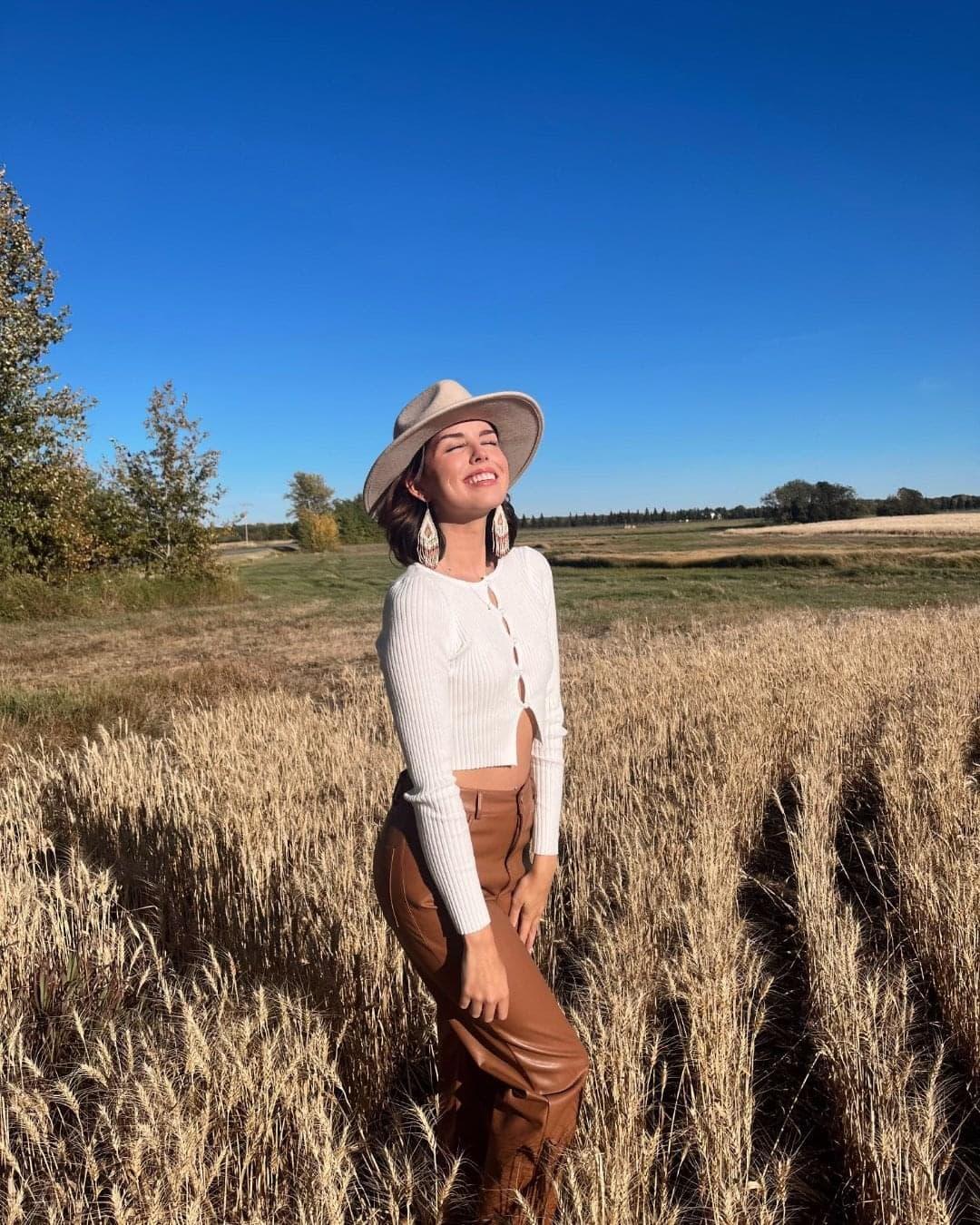Kaylee Welsh standing in a crop field, eyes closed, smiling toward the sun