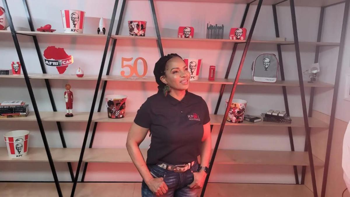 Kedibone Patricia Malatji Lebethe standing in front of a bookcase with KFC awards and memorabilia