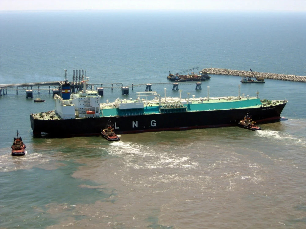 A large tanker with "LNG" on the side being pushed by smaller boats