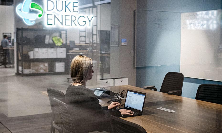 Laurel sitting alone in a conference room with glass walls, working on a laptop.