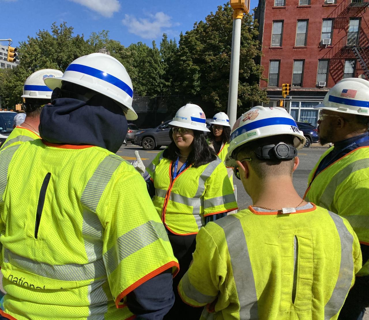 Girl stands on street corner with staff from National Grid in yellow safety vests.