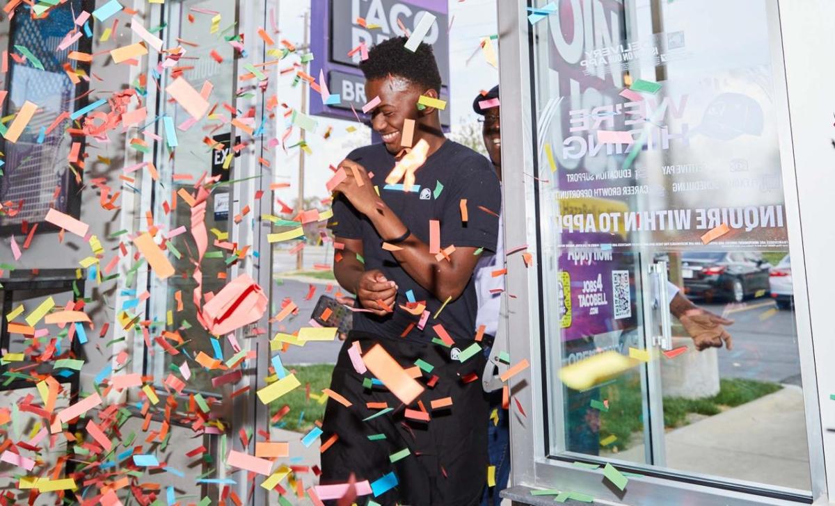 smiling person walking into a taco bell through confetti