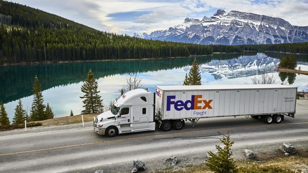 FedEx Freight truck driving past a lake with mountains in the distance