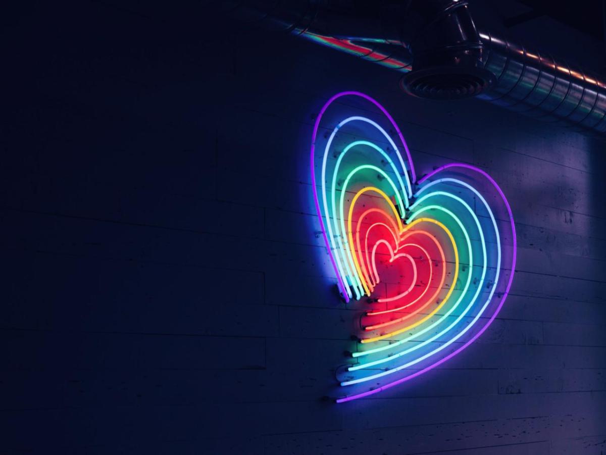A rainbow heart in neon lights on a dark wall.