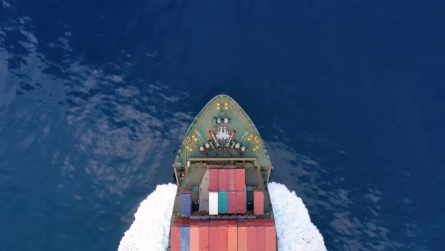 front end of a freight boat loaded with shipping containers moving through a large body of water