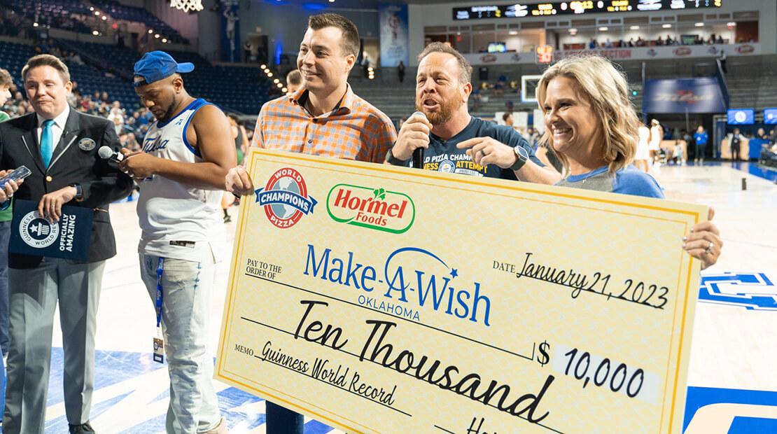 Three people holding up a giant check to Make A Wish for $10,000. Standing on a basketball court.