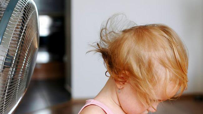 Child sits in front of a fan. 