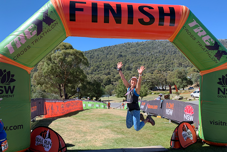 Melinda Toraya jumping with arms in the air under the finish line for the trex cross triathlon