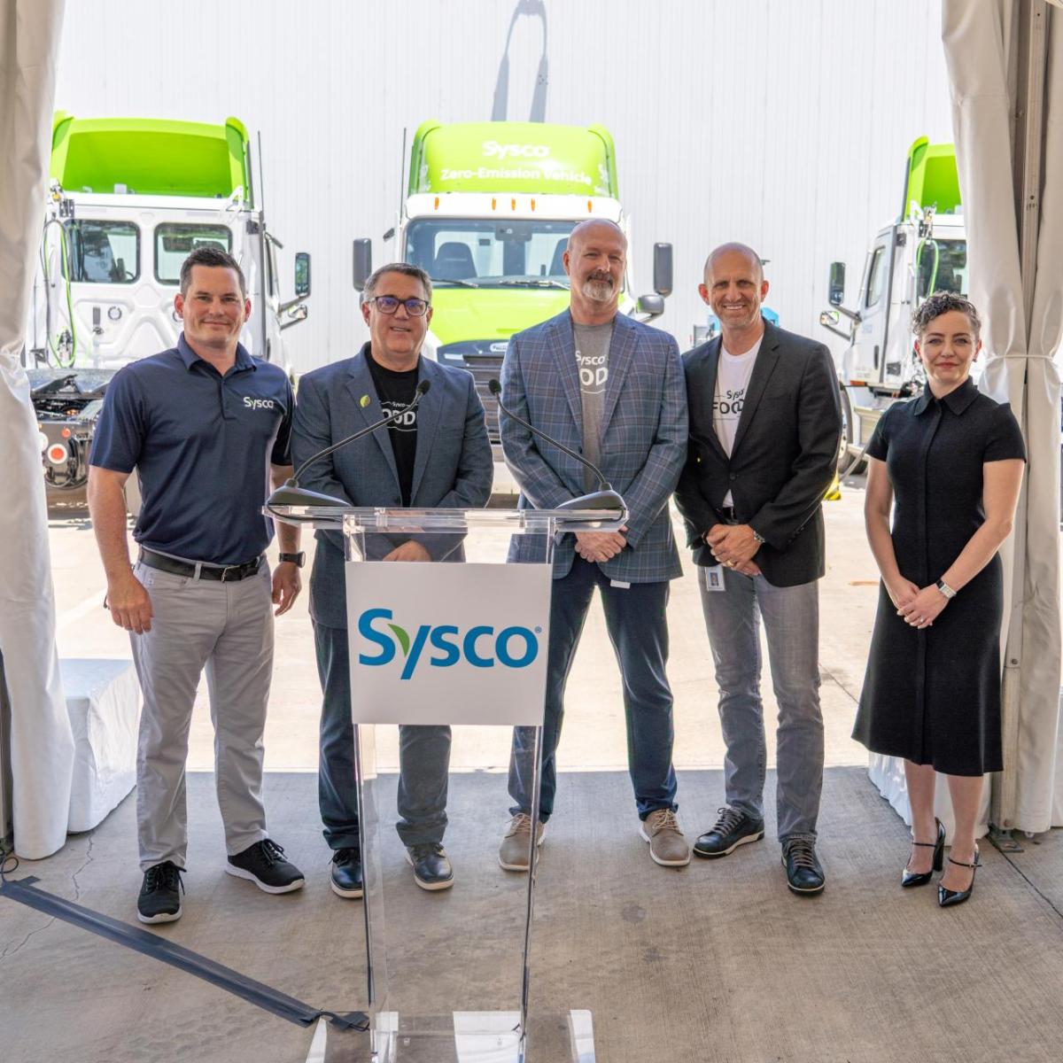 Five Sysco staffers standing in front of electric trucks. 