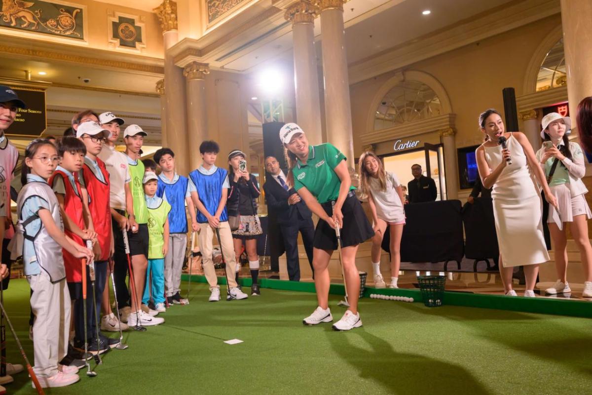 Professional golfer putting on an indoor green as others look on.