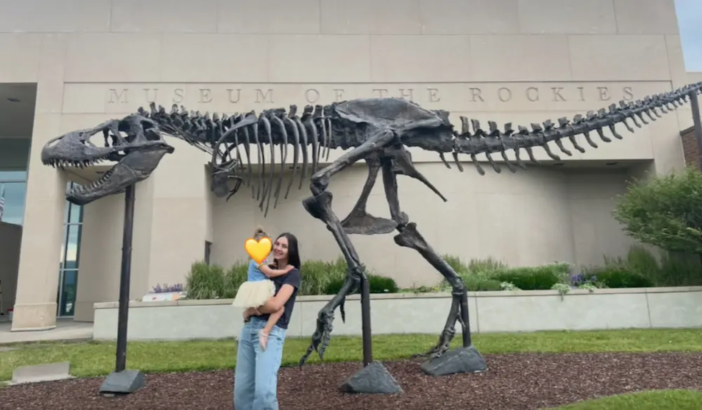 Natalie and her daughter in front of a fossil of a dinosaur.