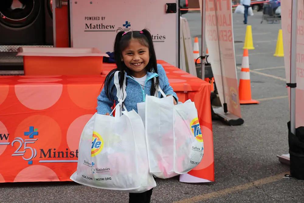 A child holding two bags with Tide logos on them, an orange table behind her.