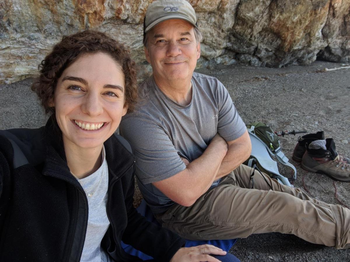 Catherine Paquette and Ned Bagno take a selfie while sitting on rocky soil. A rock wall behind them.