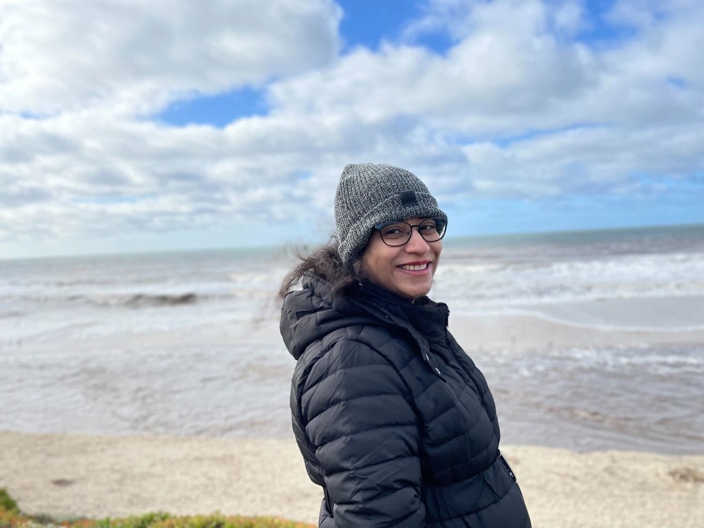 Sanjana on a cold day walking on a beach.