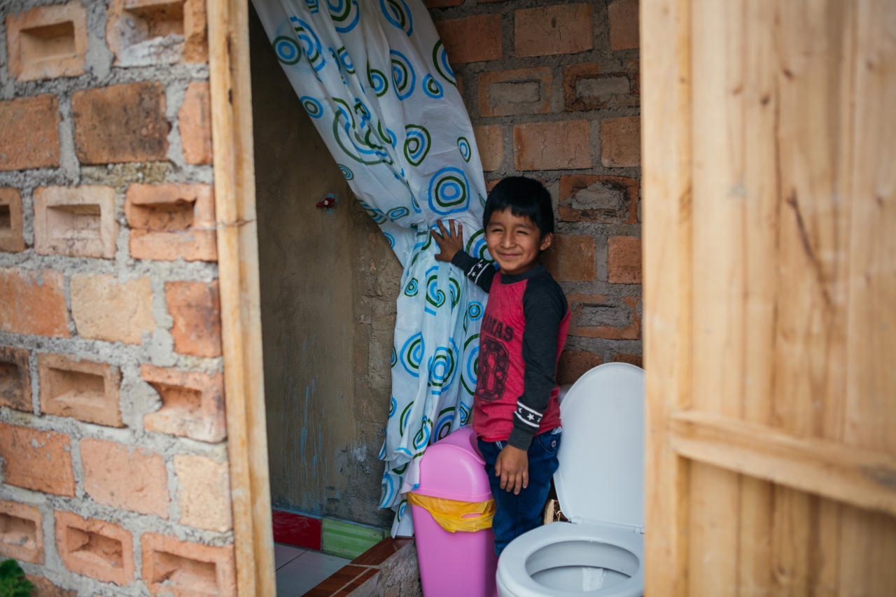 A young boy shows his family's new toilet and shower in Peru. 