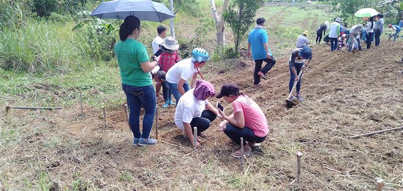 A group of community members plant crops in a field during an agriculture training session at La Cocina de Marabut in the Philippines.