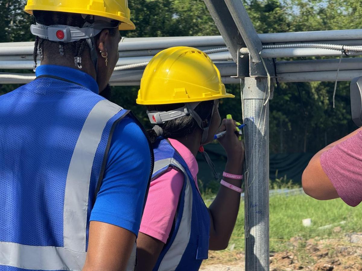 Girl in construction vest and hard hat marks greenhouse posts with permanent marker.