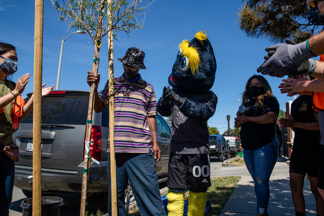 LA Galaxy mascot Cozmo and LA Galaxy and TreePeople staff congratulate a Watts resident in Los Angeles on the successful planting of a new tree in front of his home