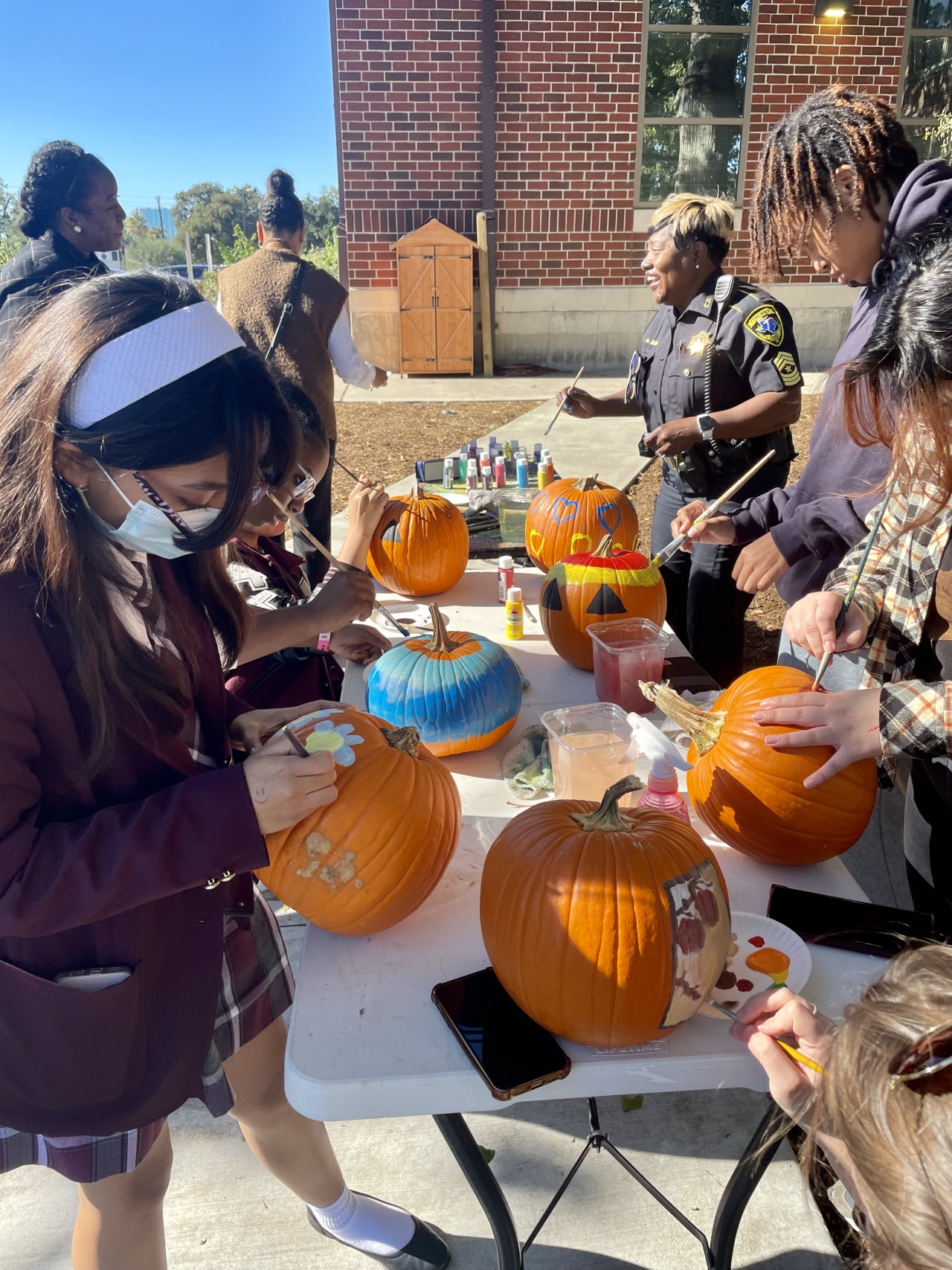 Group of high school students and police officer painting pumpkins