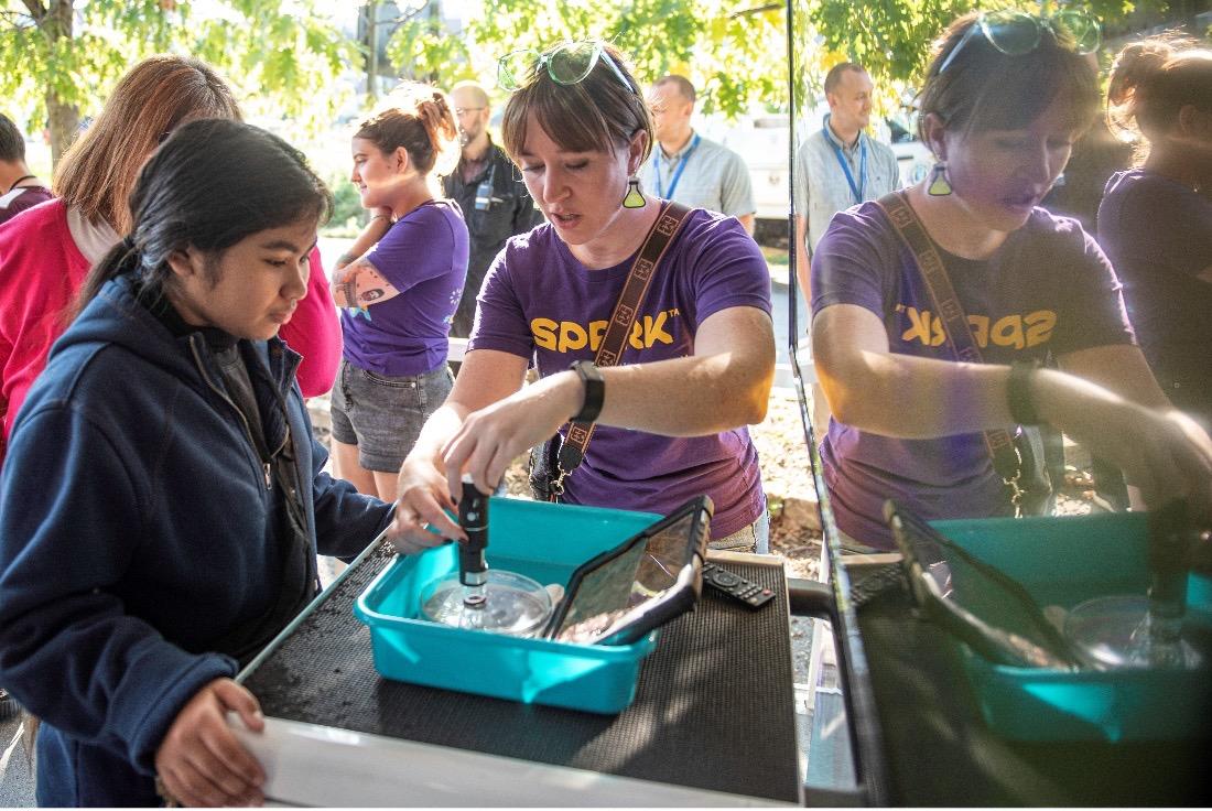 A woman in a purple SPARK MilliporeSigma t-shirt demonstrates an experiment to a student on the Curiosity Cube. 