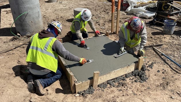 Three construction workers smoothing a square of concrete