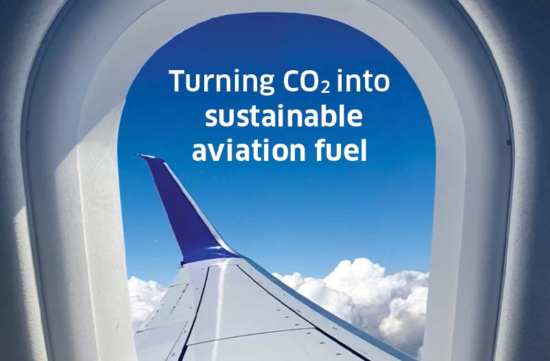 view out a plane window of the wing and "Turning CO2 into sustainable aviation fuel" in the sky