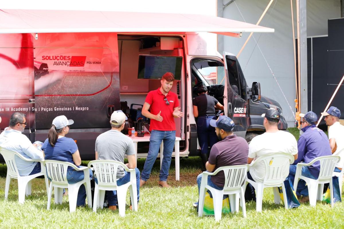A group of people in white chairs listening to a presenter, an open truck behind them with an awning, CaseIH logos.